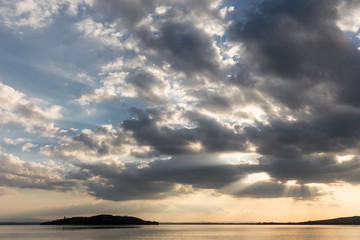 Sun rays coming out through the clouds over an island on a lake