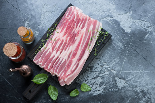 Fresh uncooked bacon with seasonings over gray stone background, horizontal shot with space, flat-lay