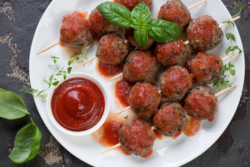Top view of baked meatballs on skewers served with tomato sauce, horizontal shot