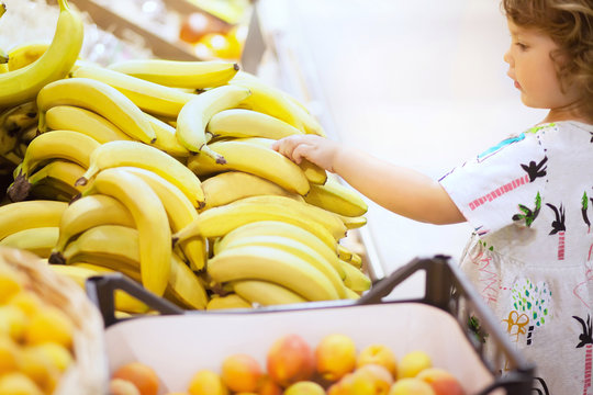 Cute Toddler Girl In A Food Store Choosing Banana Fruit