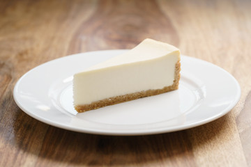 slice of traditional new york cheesecake on white plate on wood table