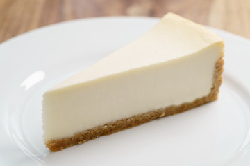 slice of traditional new york cheesecake on white plate on wood table