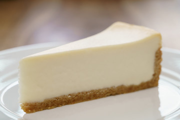 slice of traditional new york cheesecake on white plate on wood table