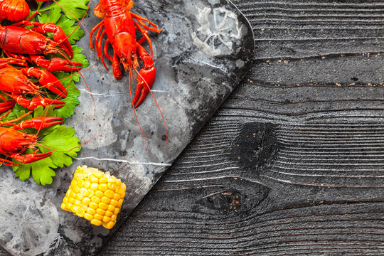 Red boiled crayfish with lemon, corn and parsley on stone slate tray on dark old rustic background. Bread with crayfish