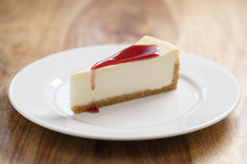 raditional new york cheesecake with berry jam on white plate on wood table