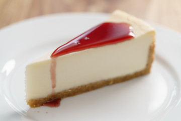 raditional new york cheesecake with berry jam on white plate on wood table
