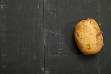Raw potatoes on a black wooden background, space for text