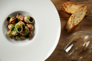 Plate with delicious snails in green sauce on wooden table
