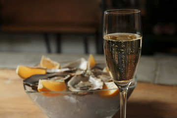 Glass with champagne and blurred oysters in bowl on background