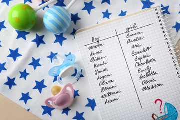 Composition with list of baby names in notebook, rattles and pacifiers on table