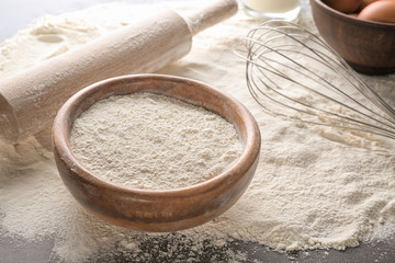 Bowl with white flour, rolling pin and whisk on kitchen table
