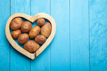 Fresh potatoes in the heart on a blue wooden background