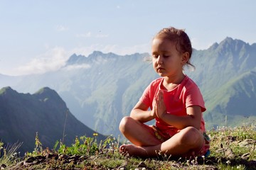 Little cute girl meditating on top of mountain