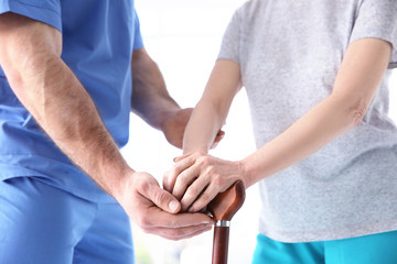 Obraz premium Elderly woman and young man holding hands on walking stick, closeup. Physiotherapy concept