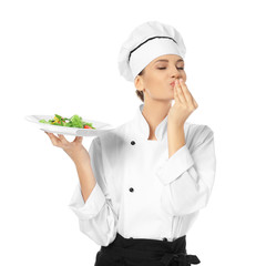 Young female chef holding plate with salad on white background