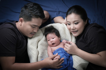 family portrait of young asian mum and dad and boy newborn in black background .