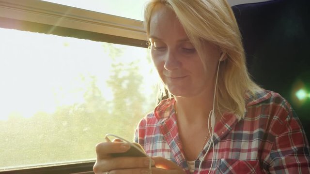 A young woman is traveling on a train using a smartphone. The sun's rays blink on her face