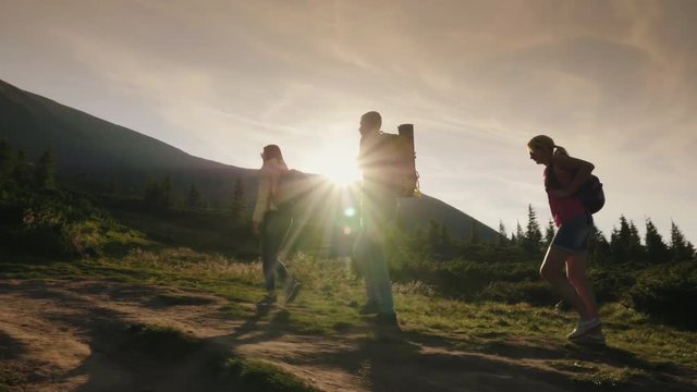 A group of friends with backpacks rises up the mountain. In the rays of the setting sun. Active lifestyle