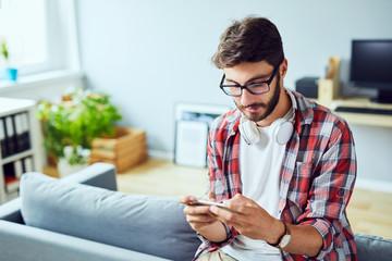 Young man leaning on sofa and playing games on phone at home