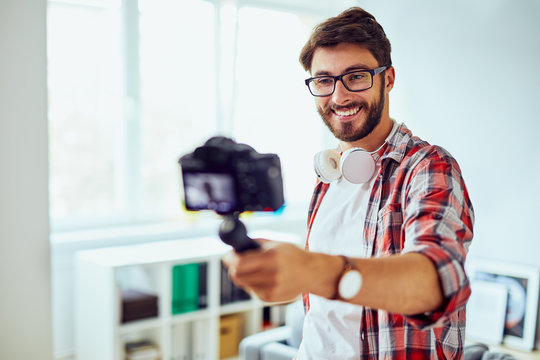 Young smiling man making vlog with handheld camera in his home