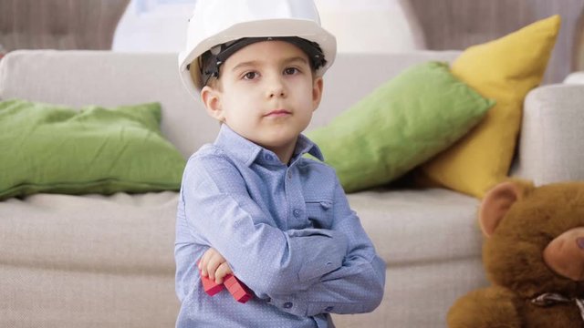 small kid boy imitates engineer constructing a building using colorful meccano details with enthusiasm and focus dreaming about future profession, sitting at home on floor
