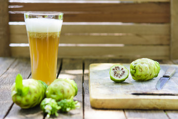 Noni fruit and Noni slice with knife on chopping board and noni juice on old wooden table