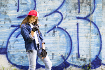 Cute young fair-haired girl teenager in a baseball cap and denim shirt on a stone wall background.