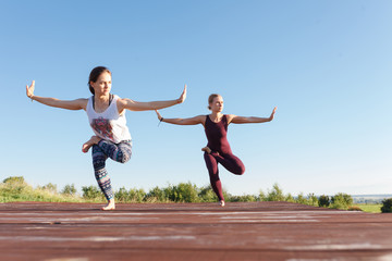 Two Young yoga woman practitioners in group doing yoga on nature at sanny day with blue sky