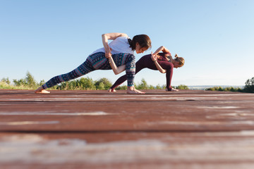 Two Young yoga woman practitioners in group doing yoga on nature at sanny day with blue sky