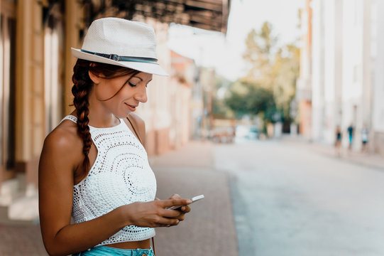 Stylish woman with hat using phone outside.