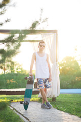 Obraz premium Young male wearing a blank white t-shirt and shorts with sunglasses and skateboard. A skater with a board is standing on a green park background at sunset