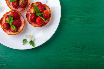 Strawberry tartlet on white plates on green background. Top view.