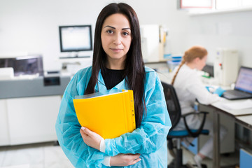 Attractive female lab worker making medical research in modern laboratory. Scientist holding documents folder with analysis results.