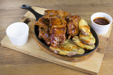 Delicious barbecued ribs seasoned with a spicy basting sauce and served with chopped potato on a wooden chopping board in a restaurant.