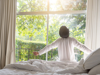 lazy man happy waking up in the bed rising hands to window in the morning with fresh feeling relax