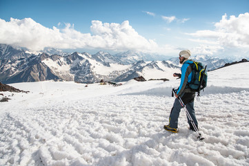 Fototapeta na wymiar The tired traveler descends from the snowy top against the background of snow-capped mountains