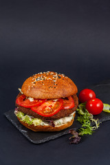 Craft beef burger with tomatoes on black table isolated on black background.