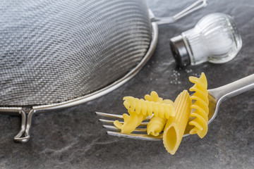 Nudelsorten auf Gabel, Nudelsieb und Salzstreuer auf schwarzem Granit, Hintergrund