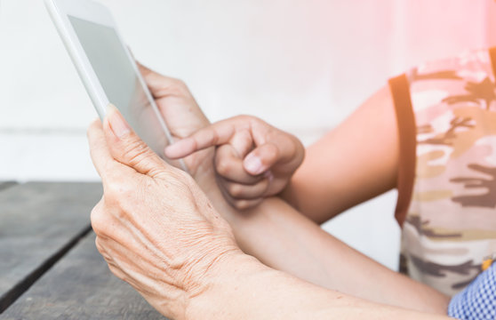 Close Up Of Grandparent Hands Using Tablet And Child Hand Point To The Screen, Technology With Senior People