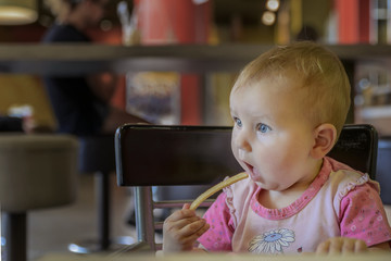 Little cute baby eat fried potatoes in a restaurant