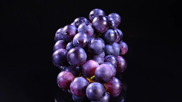 Bunch of ripe red grapes with drops of water rotates on black mirror background in 4K. Closeup view shot.
