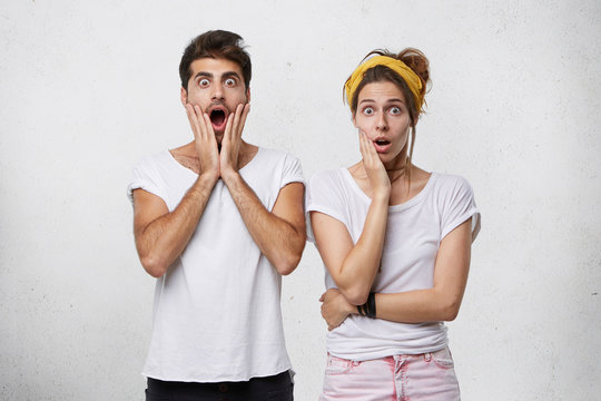 Human emotions and feelings. Astonishment and surprise concept. Studio shot of astonished young Caucasian couple or family in casual clothing screaming, looking at camera in shock and full disbelief