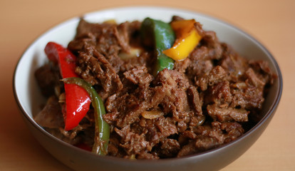 Black pepper beef in bowl with wood background.