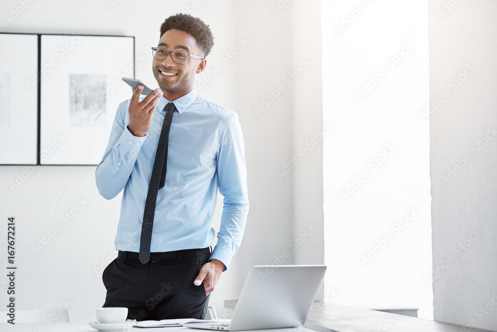 Wall mural elegant manager with dark skin, wearing white shirt with tie and black trousers, standing in private