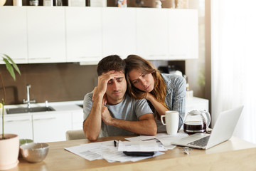 Stressed wife and husband with many debts doing paperwork together, reviewing their expenses,...