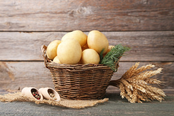 Potatoes in wicker basket with pepper and wheat ears on wooden background
