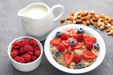 Oatmeal in plate with berries, nuts and jar of milk on wooden table