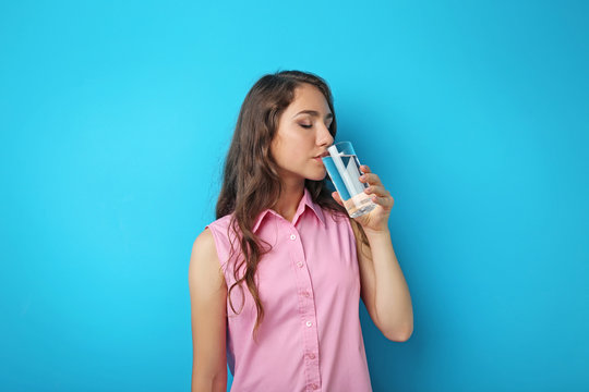 Portrait of young woman with glass of water on blue background