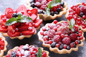 Dessert tartlets with berries and powdered sugar on grey wooden table