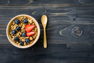 Homemade granola and fresh berries on wood table with space.